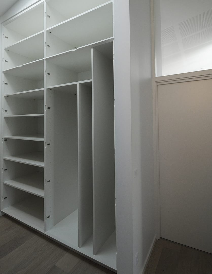 Indbygget skabsvæg med lodrette hylder til stige, strygebræt med videre. Personlige løsninger fremstilles hos Jesper Holm Design i København.
